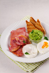 Bacon, poached eggs, mashed peas and toasts on white plate. Grilled rashers and eggs