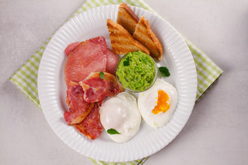 Bacon, poached eggs, mashed peas and toasts on white plate. Grilled rashers and eggs