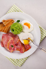 Bacon, poached eggs, mashed peas and toasts on white plate. Grilled rashers and eggs