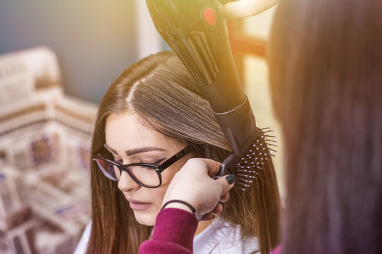 Close-up of a woman getting her hair dried. Beautiful young girl at the hair salon. Hairdresser holding a hairdryer.