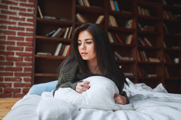 Beautiful sad brunette woman in a green sweater lies on a bed