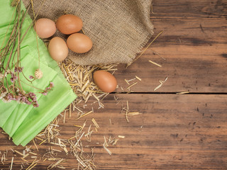 Rural creative background with brown eggs, burlap, straw, green paper and dry flowers on wooden table from old planks. Vintage, rustic background for Easter postcards, restaurant menus or advertising
