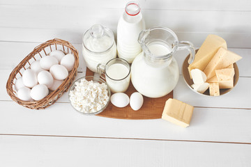 Top view of a set of products consisting of milk, butter, curd, cheese and eggs on white wooden table