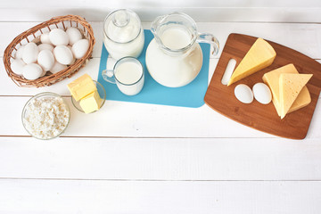Top view of a set of products consisting of milk, butter, curd, cheese and eggs on white wooden table