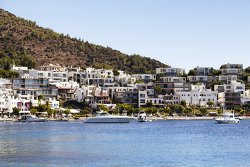 Fototapeta na wymiar View of yachts and Icmeler area of Bodrum city. White summer houses reflects region's architectture style. It's a calm, hot summer day.