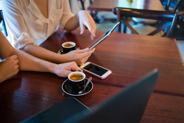 Close up of two female model's hands using smart devices while having coffee in a coffee shop as part of their business meeting