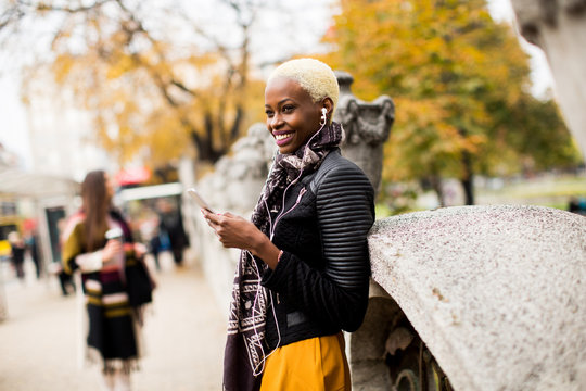 African american and caucasian woman posing outside with mobile phone and a cup of coffee to go in autumn