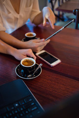 Close up of two female model's hands using smart devices while having coffee in a coffee shop as part of their business meeting