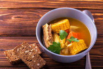 Puchero soup with corn and parsley on wooden table