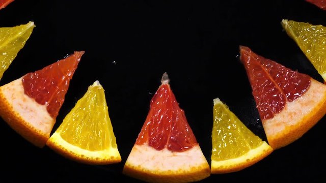Excellent top view of fresh orange and red grape-fruit sector slices, put in ring on black dish, rotating clockwise with up center. Flat lay of dessert on dark background with amazing texture in 4k.