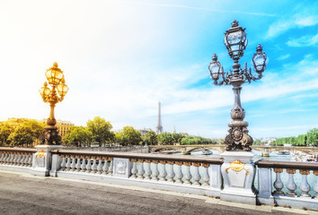 Fototapeta na wymiar Alexandre III bridge over the river Seine with the Eiffel tower in the background in Paris, France. Decorative lamp at foreground. Dramatic sky at background with opposite colors - yellow and blue.