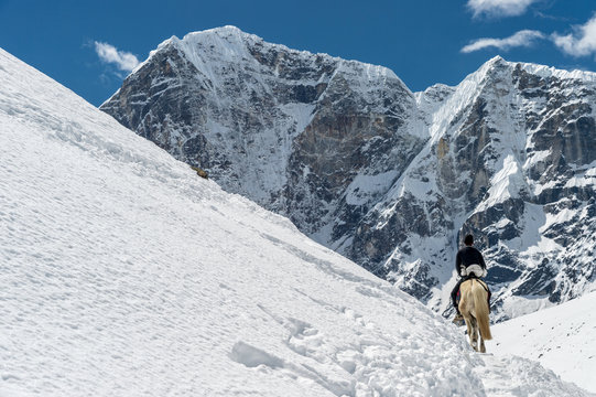 A sherpa is riding a horse with high mountains in the background (Khumbu Region, Nepal)