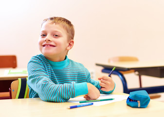 cute boy with special needs writing letters while sitting at the desk in class room
