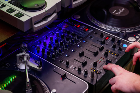 Close up Dj hands on equipment deck and mixer with vinyl record at party