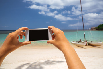 Phone smartphone in the hands of a girl on the background of the beach and yachts. A girl is making a photo on a white smartphone yacht on a tropical beach.