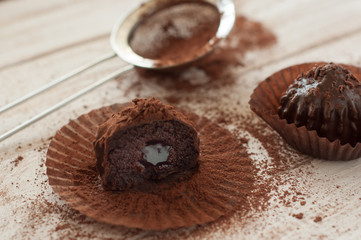 Chocolate chip muffin in brown wax paper. Unwrapped. Cocoa powder in the background