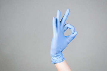 Blue latex medical gloves on a female hand, shows the character okay