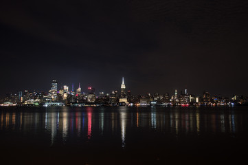 Fototapeta na wymiar Midtown and Downtown Manhattan Lit Skyline Reflecting in the Hudson at Night as Seen from Newport Green Park in Jersey City, USA