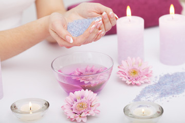 Fototapeta na wymiar Spa Manicure. Woman Hands With Perfect Natural Healthy Nails Soaking In Aroma Hand Bath. Closeup Of Glass Bowl With Water And Blue Sea Salt For Spa Procedure. Professional Nail Care. High Resolution