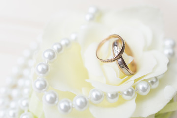 Wedding rings on a flowers with pearls on a wood background