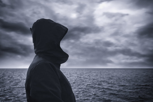 Faceless hooded person looking at horizon over sea water