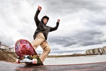 Fototapeten Teen skater in a hoodie sweatshirt and jeans slides over a railing on a skateboard in a skate park © yanik88