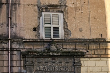 Window with white shutters in a very old house. House in emergency condition. Facade with cracks and holes needs repair