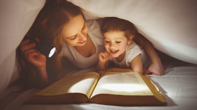 Mother and child read book under blanket with a flashlight.