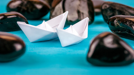 Couple of White Paper Ships between Abstract Black Rock Stones on Blue Background