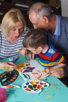 Grandmother and grandfather with grandson drawing together at home.