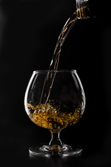 brandy or whiskey pouring into glass on a black background