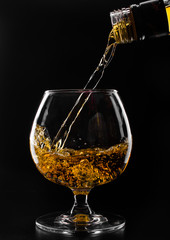brandy or whiskey pouring into glass on a black background