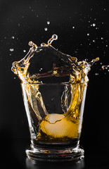 A glass of whiskey and ice cube on a black background