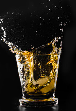 A glass of whiskey and ice cube on a black background