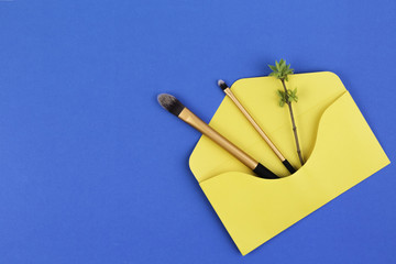 Make up brushes with spring gentle leaves and buds on small tree twigs in yellow envelope on blue background