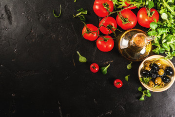 Ingredients of Italian cuisine. Selection of products for salad. Olive oil, lettuce leaves, tomatoes. On a black dark shale concrete stone kitchen table. copy space top view