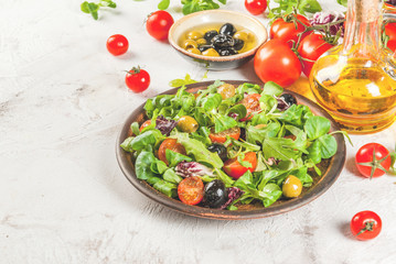 Italian Cuisine. Spring vegan diet food. Fresh lettuce, greens, tomatoes, green and black olives. With fresh organic home-made oil, raw ingredients on the table. Copy space 