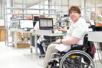 Rollstuhlfahrer am Arbeitsplatz in einer Fabrik zur Montage von Elektronik - Alltag mit...