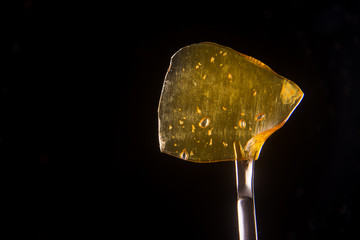 Cannabis oil concentrate aka shatter held on a dabbing tool over black
