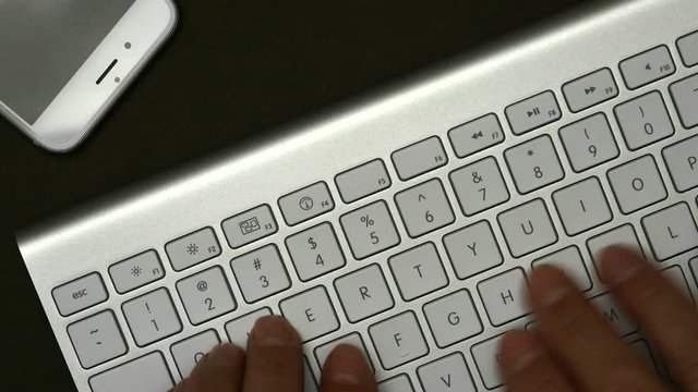 Elderly Man Is Typing On A Keyboard. On The Table Is A Mobile Phone.