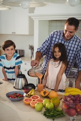 Father preparing smoothie with his kids in kitchen