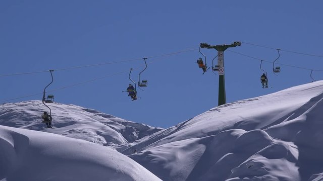 Unrecognizable people on ski chair lift riding up to the mountain peak for downhill skiing