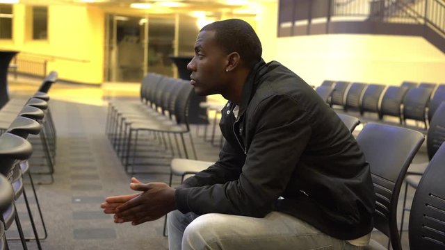 Young male in auditorium with lots of empty chairs surrounding him.
