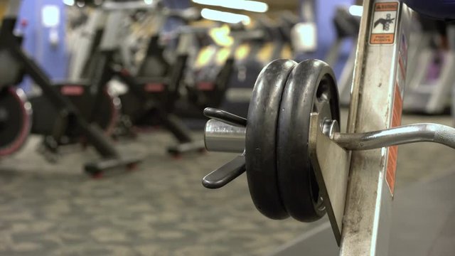 Person walking by in background of gym weight at preacher curl bench.
