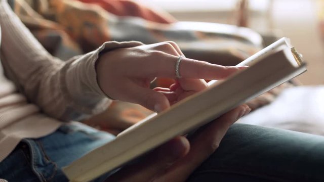 close up view of paper book in hands of latin beautiful young woman who read and studying it with interest, leaf pages with fingers, sitting on leather sofa in the room during sunny day