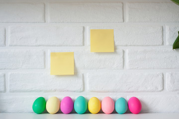 Easter colored eggs with sticky note paper against white brick wall background. Cute Easter celebration decoration. Copy space for text.  Happy Easter card. Easter concept.