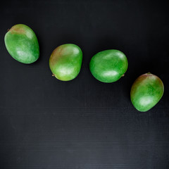 Green mangos on black background. Flat lay, top view. Fruit background