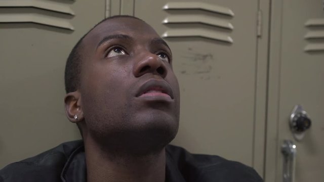 Depressed African American male high school student in front of school locker.