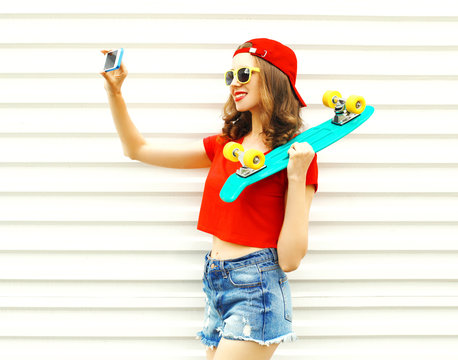 Fashion pretty cool smiling girl doing self portrait on smartphone over white background