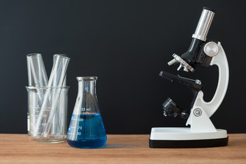 science laboratory test tubes and white microscope on wooden table with black background , laboratory equipment